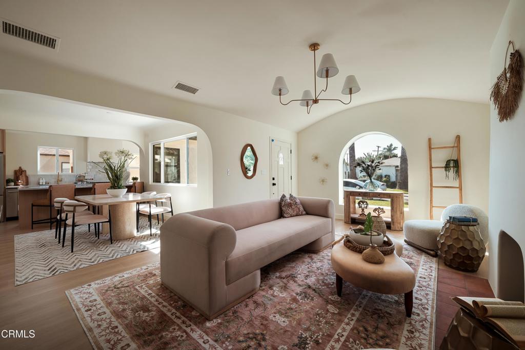 Living room with a blush sofa and patterned rug, opening onto a dining area and kitchen.