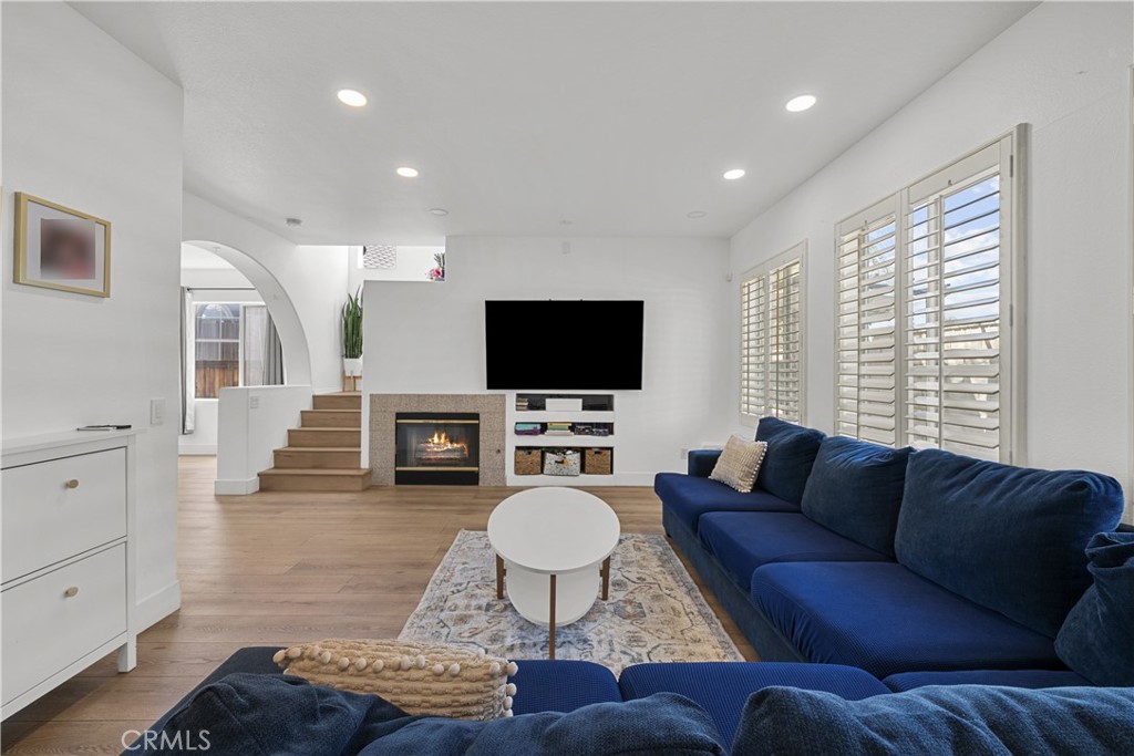 Living room with a navy sectional, fireplace, wall-mounted television, and plantation shutters.