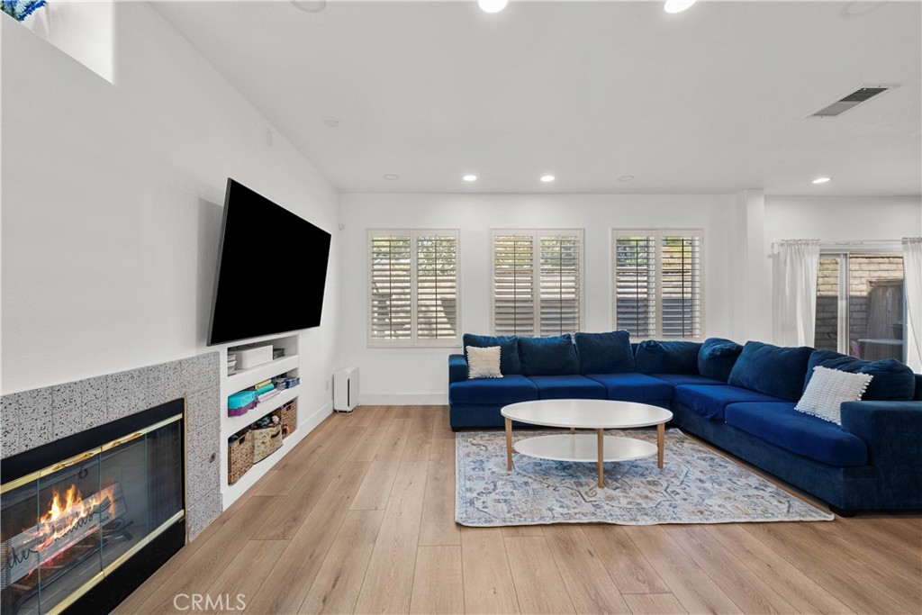 Living room with a blue sectional, plantation shutters, wall-mounted television and modern fireplace.