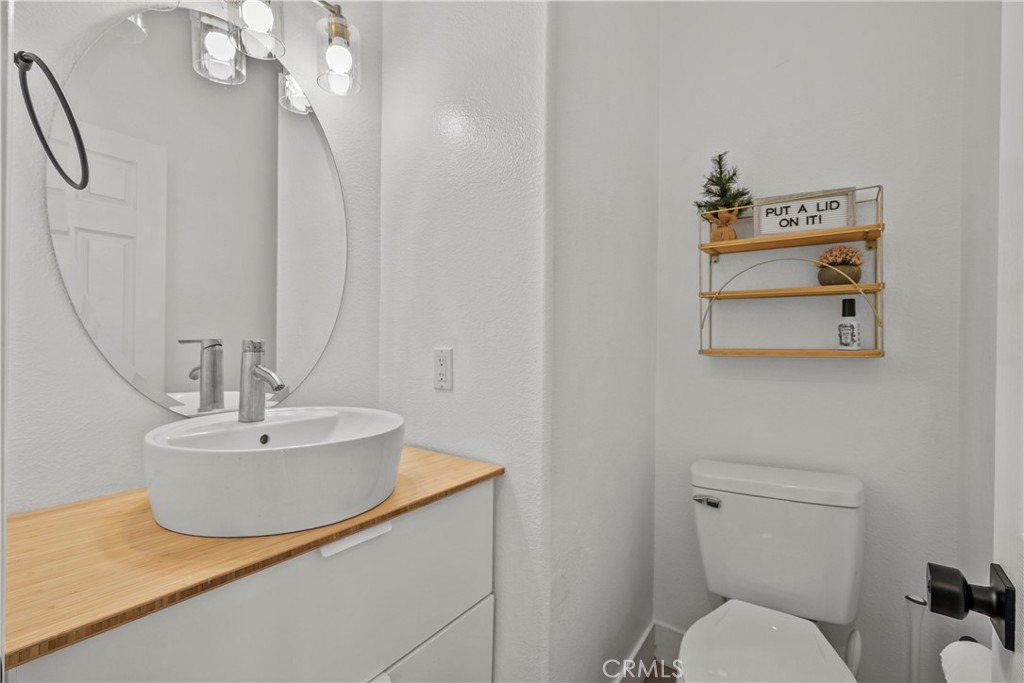 Bathroom with a white vessel sink on a wood countertop and a decorative shelf above the toilet.