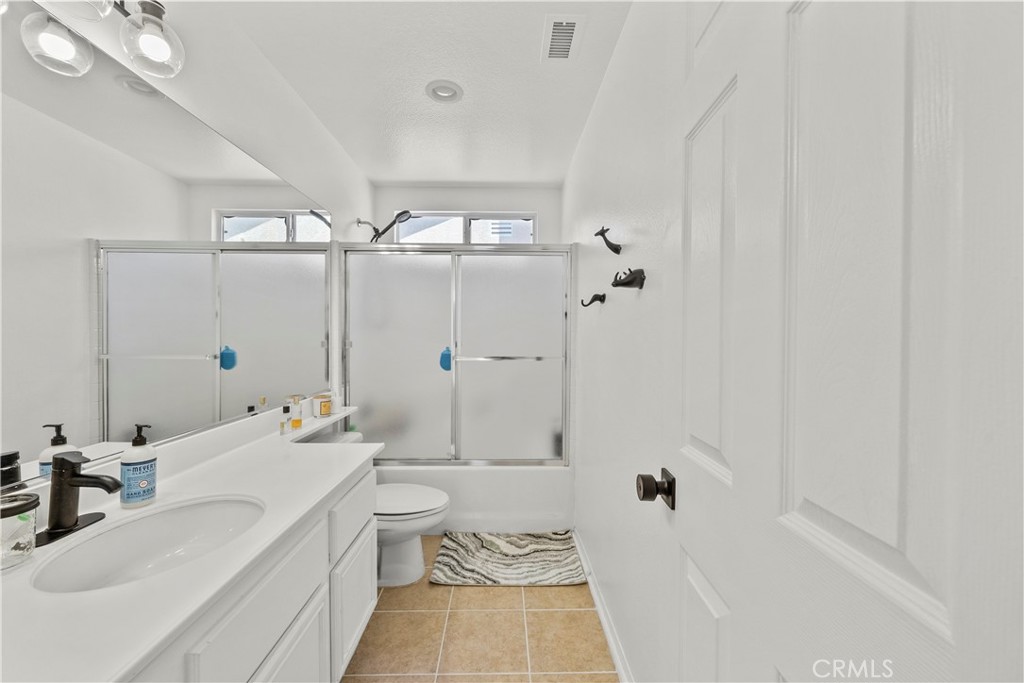 Bathroom with a white vanity, frosted-glass shower doors, and tan tile flooring.