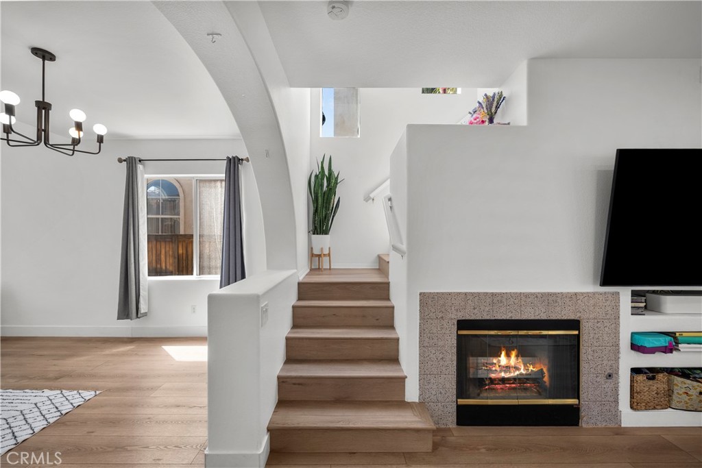 Living room with a wooden staircase beside a lit fireplace and light wood floors.