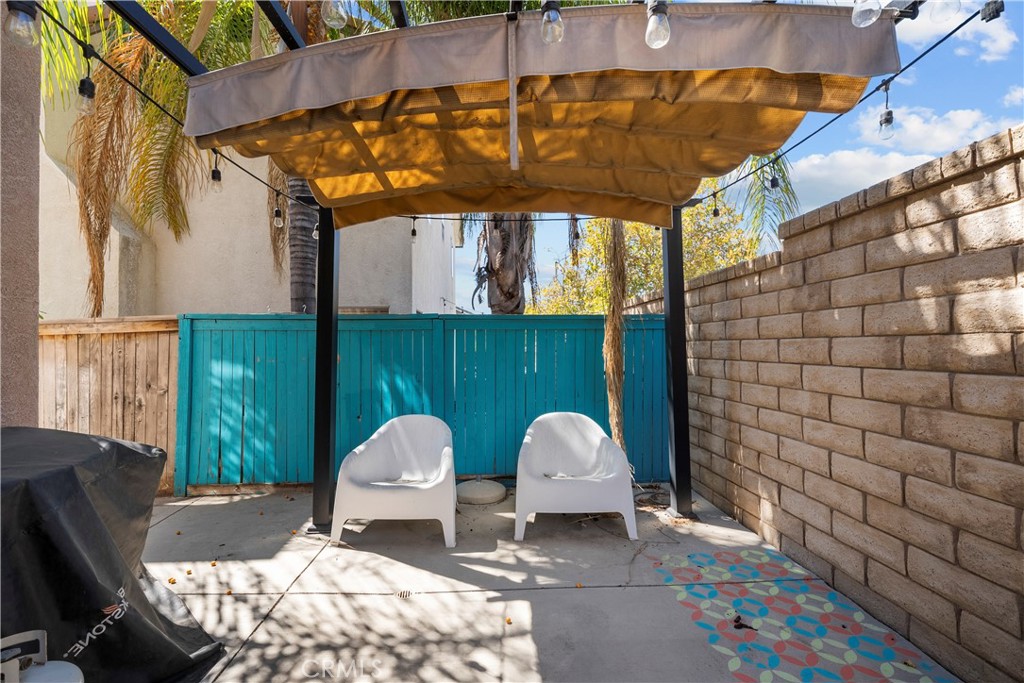Backyard patio with a canopy, two white chairs, turquoise fence, and covered grill.