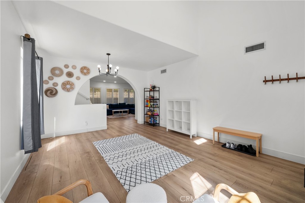 Open living area with light wood floors, a geometric rug, and an arched opening to a sitting room.