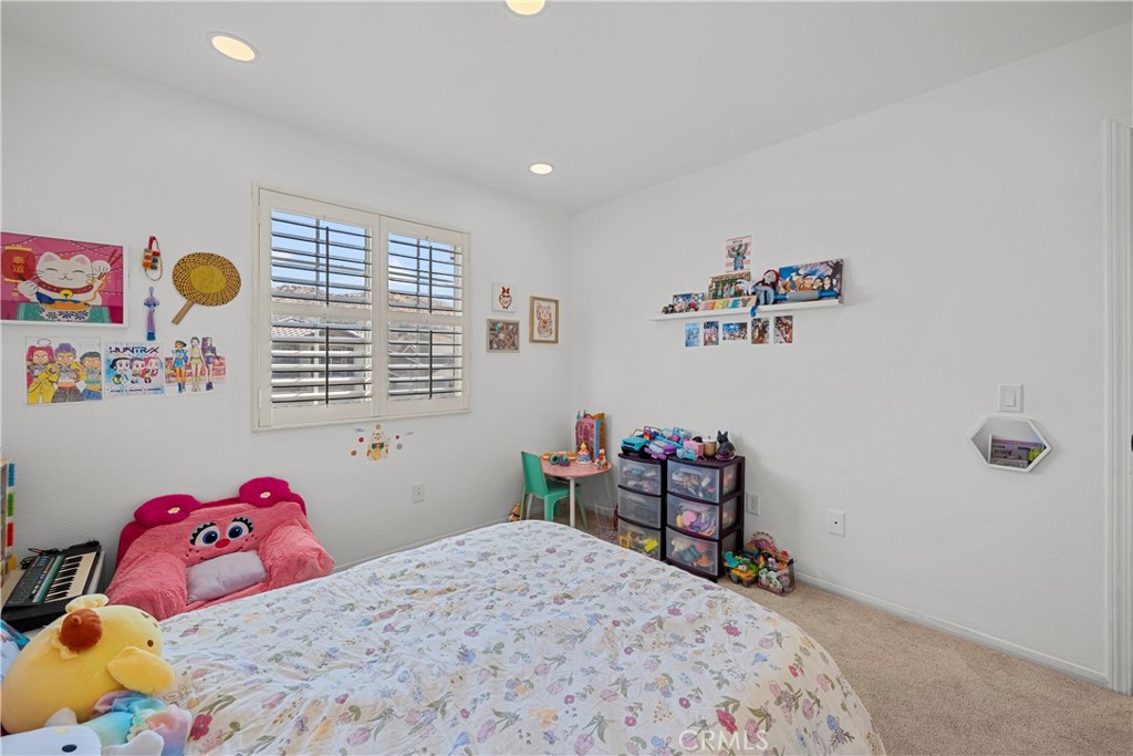 Bedroom with a floral bedspread, plush toys, children’s artwork, and shuttered windows.