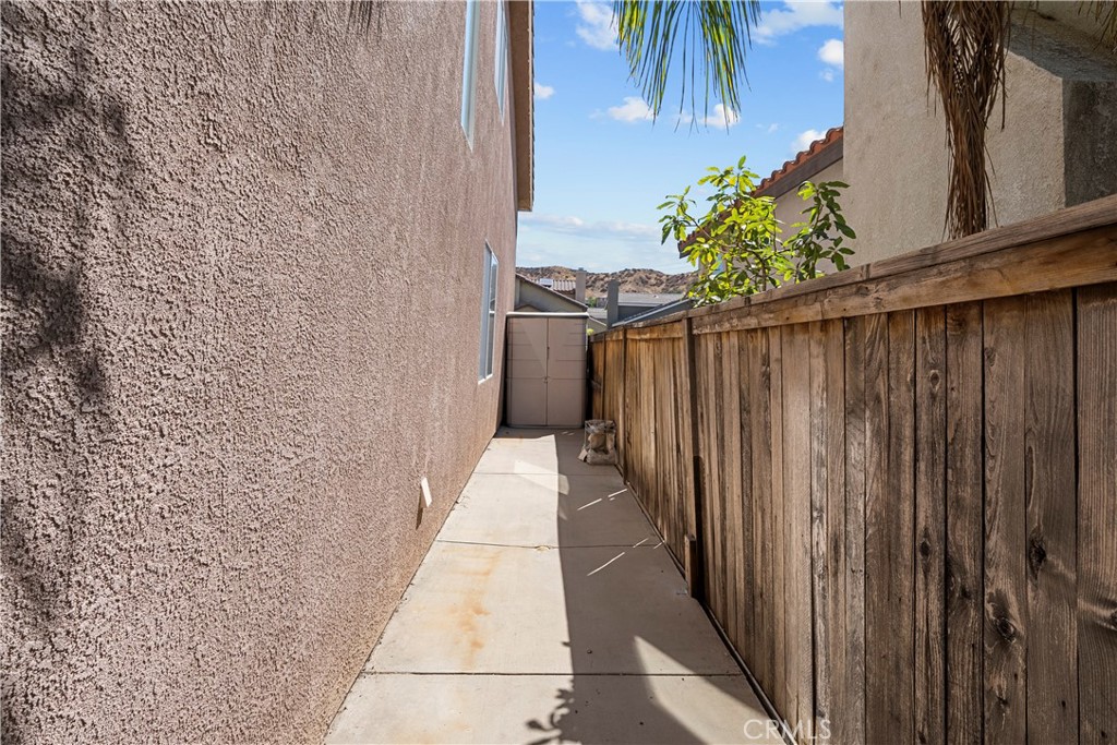 Concrete side yard with a tall wooden fence and a small storage shed.