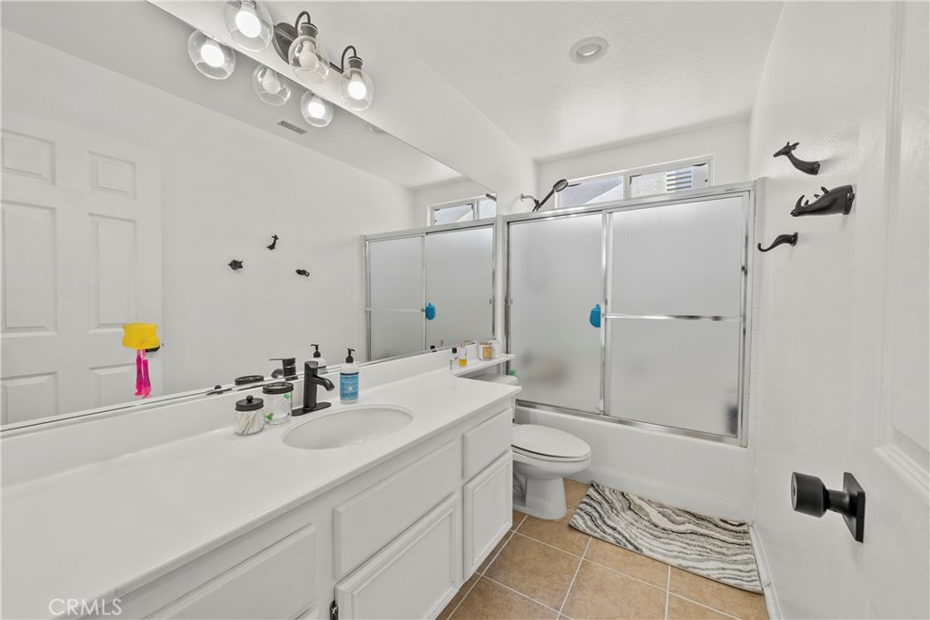 Bathroom with a long white vanity, tan tile floor, and frosted glass tub enclosure.