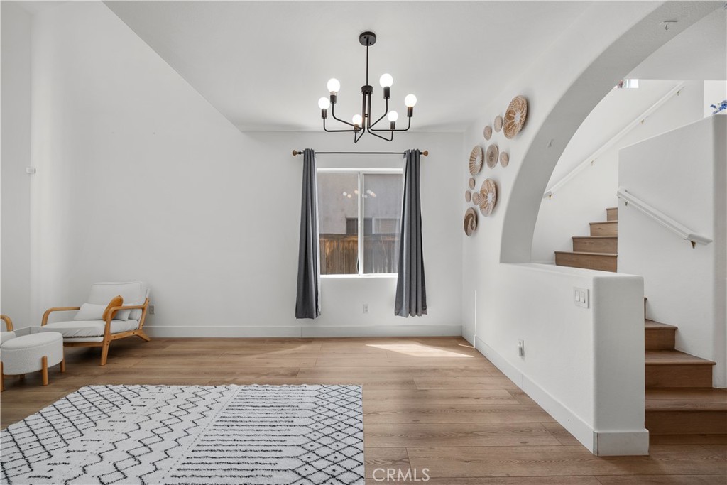 Staged living room with wood floors, a patterned rug, and a staircase beneath an archway.