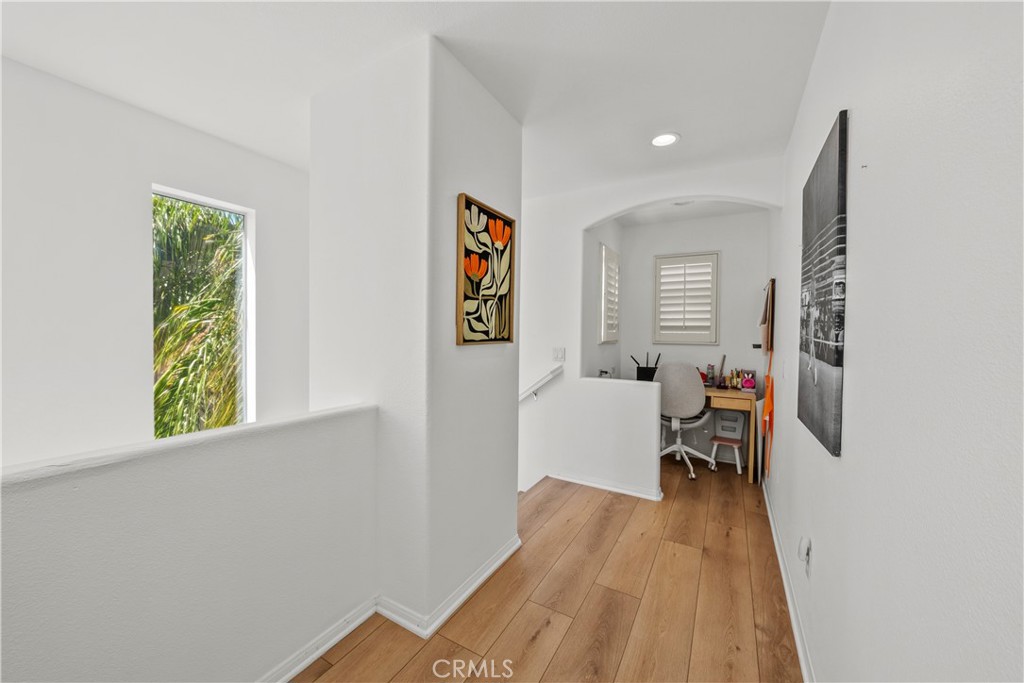 Bright upstairs hallway with wood floors leading to a small desk nook and shuttered window.