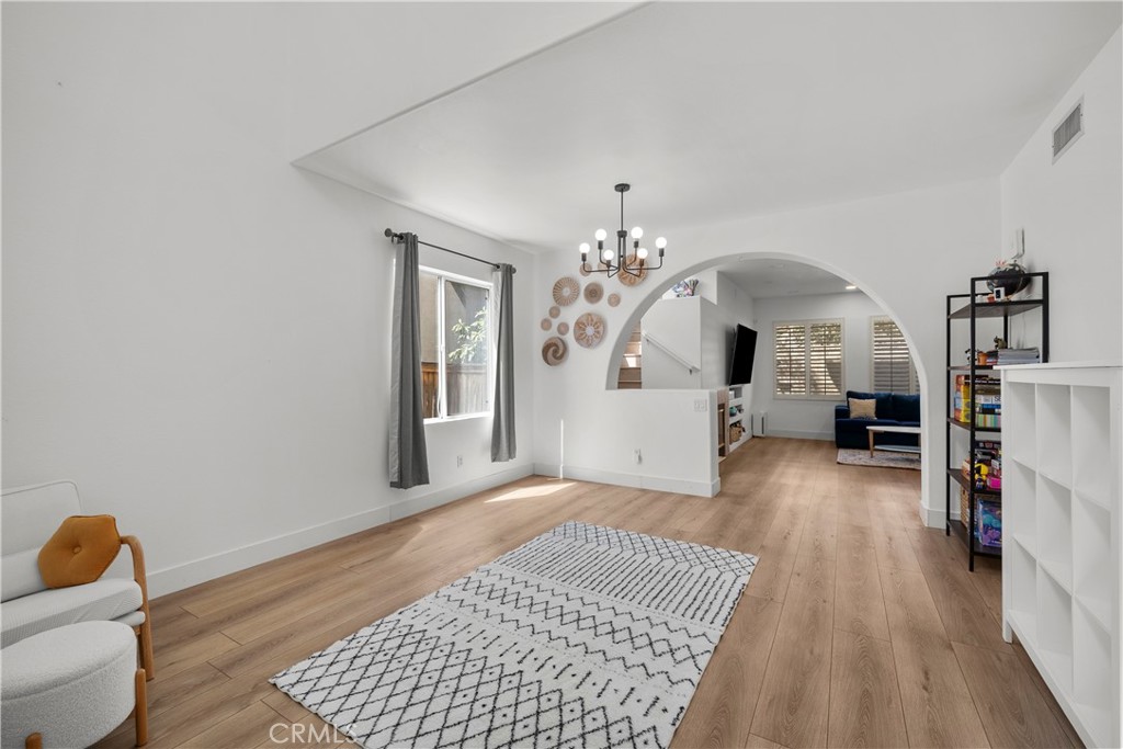 Staged living room with wood flooring, patterned rug, chandelier, and arched opening to a sitting area.