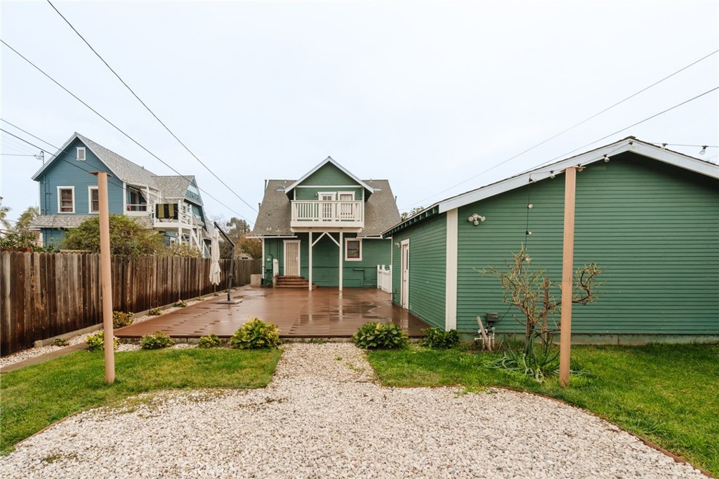 Green house and outbuilding behind a gravel path, with a raised wooden deck and landscaped backyard.