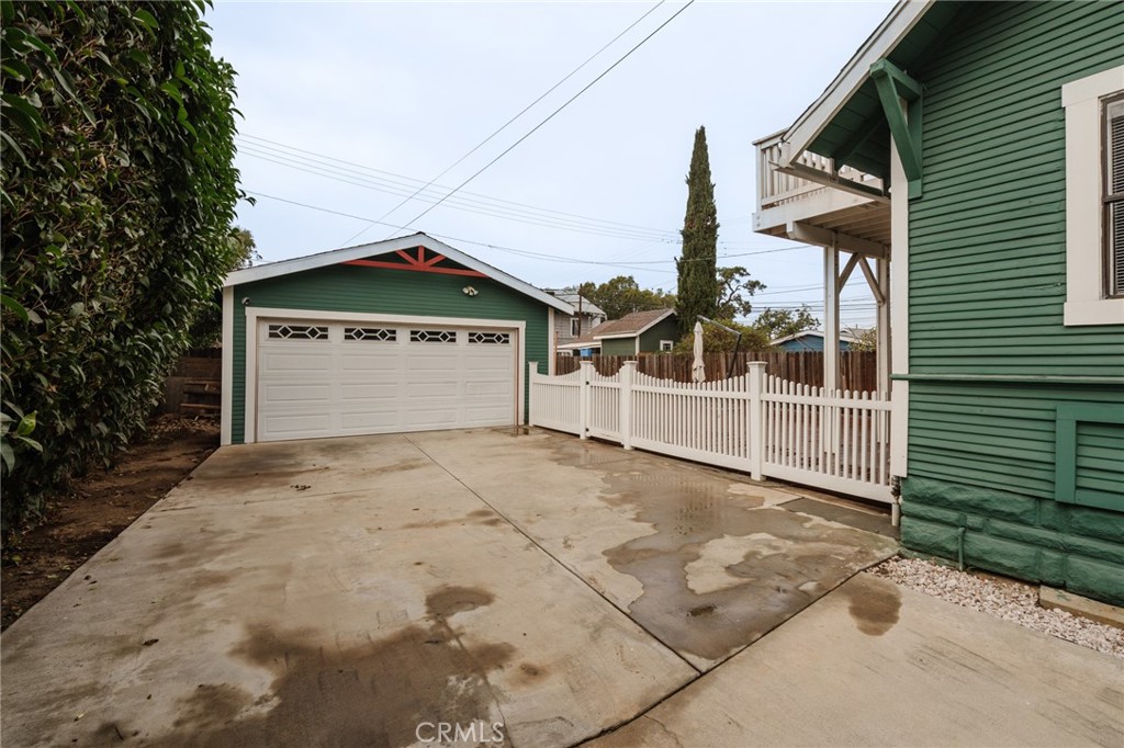 Green detached garage and concrete driveway beside a house, with a white picket fence.