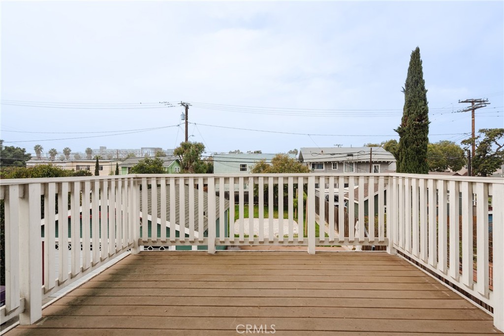 Wooden deck with white railings overlooking neighborhood rooftops and a tall cypress tree.