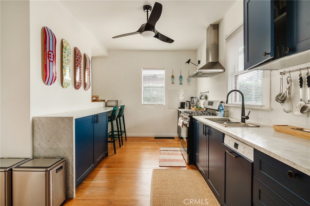Narrow kitchen with navy cabinets, stone counters, wood floors, and skateboard decks on the wall.