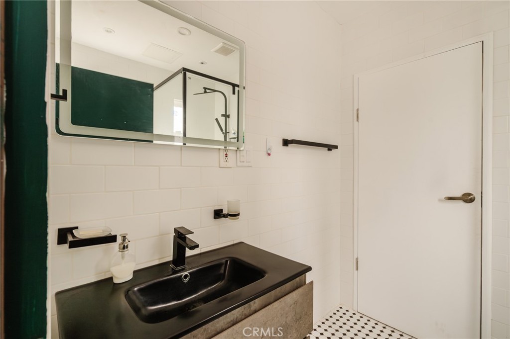 Bathroom with a black vanity sink, large mirror, white tile, and patterned floor.