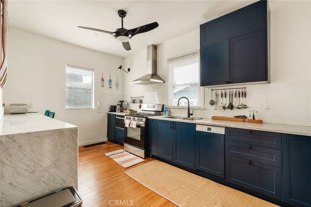 Kitchen with navy cabinets, a marble island, stainless steel range, and wood floors.
