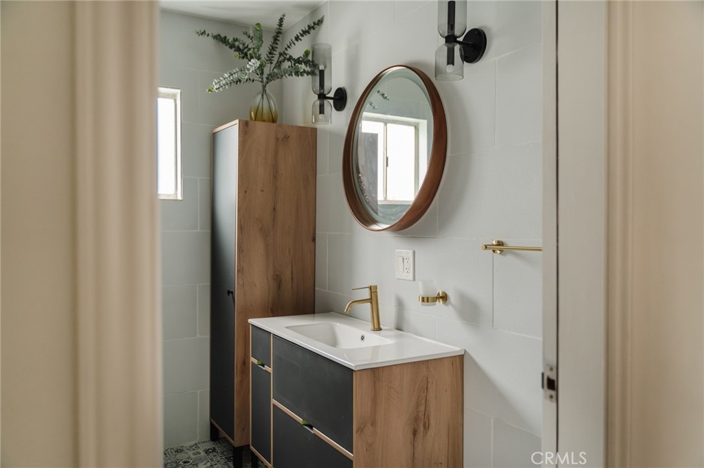 Bathroom with a wood-and-charcoal vanity, brass fixtures, round mirror, and tall cabinet.