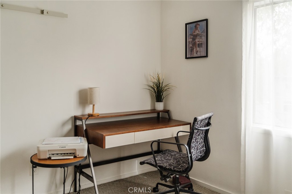 Home office with a wooden desk, patterned chair, printer, and bright window.