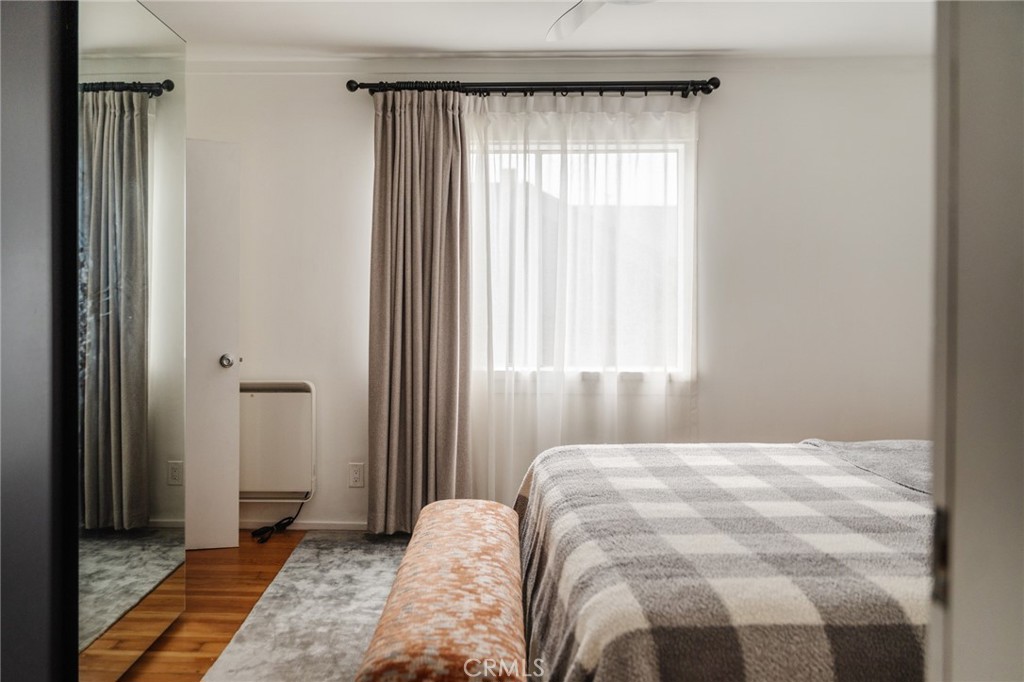 Bedroom with a checkered bedspread, sheer-curtained window, and mirrored closet door.
