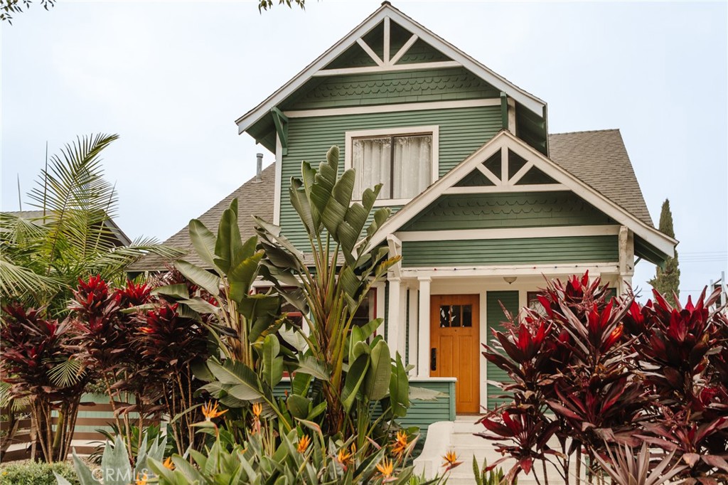 Green gabled home with white trim, an orange front door, and dense tropical landscaping.