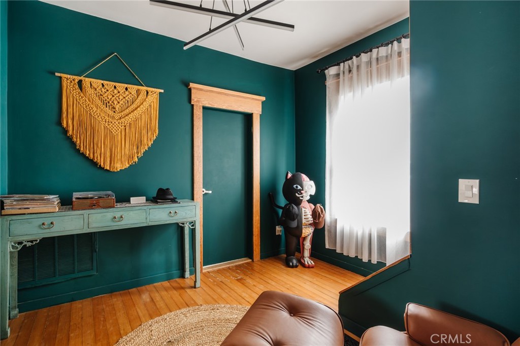 Teal-walled living room with hardwood floors, a macramé wall hanging, and figures beside a bright window.