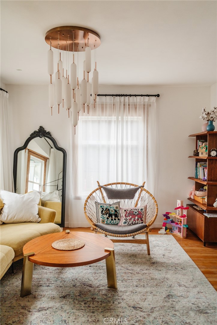 Living room with a yellow sofa, woven chair, round wood coffee table, and sculptural pendant light.