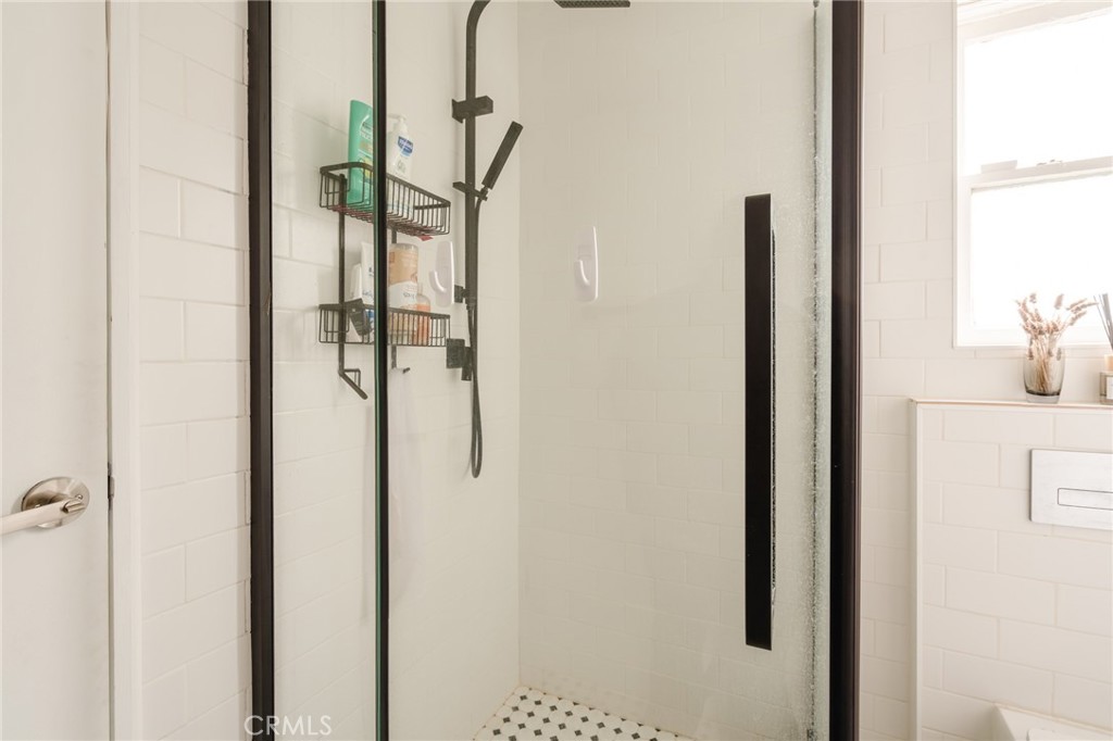 White-tiled bathroom shower with black-framed glass enclosure, black fixtures, and mosaic floor.
