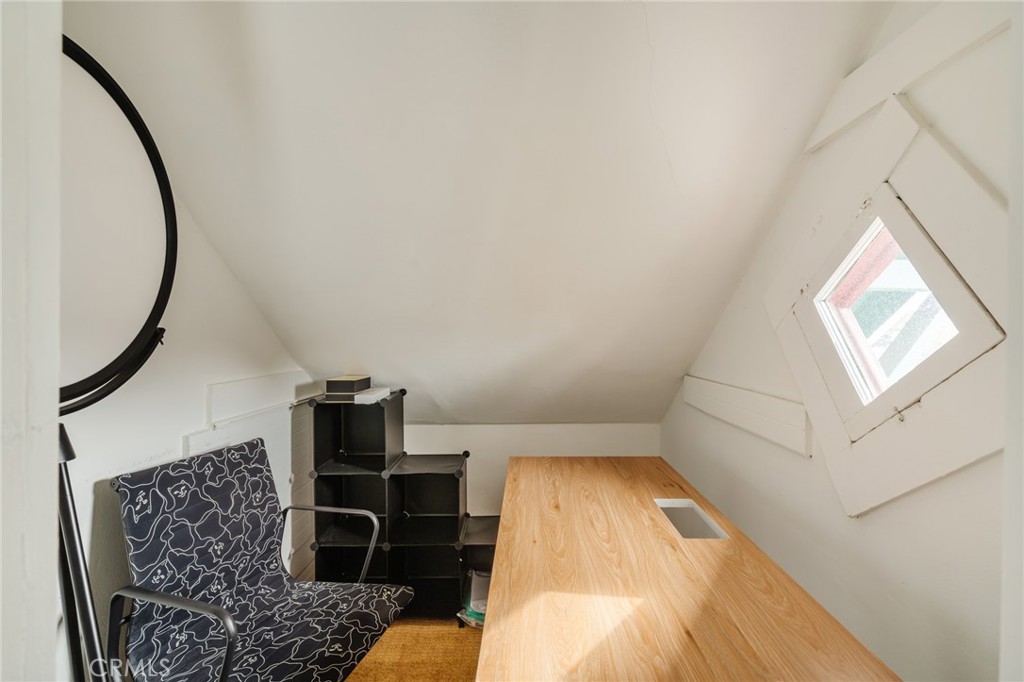 Attic office with a long wooden desk, patterned chair, and small angled window.