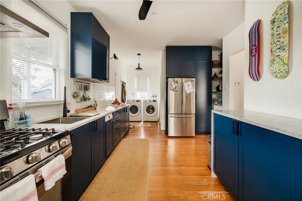 Kitchen with dark blue cabinets, stainless steel appliances, wood floors, and a washer and dryer.