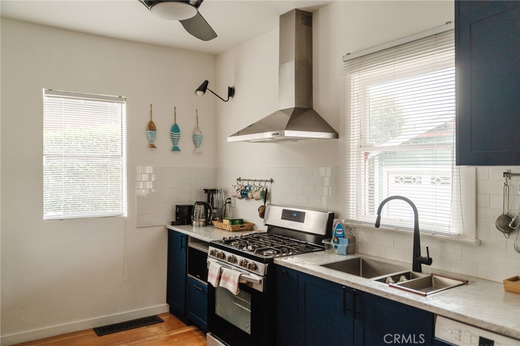 Kitchen with navy cabinets, stainless-steel range hood, white tile backsplash, and double-basin sink.