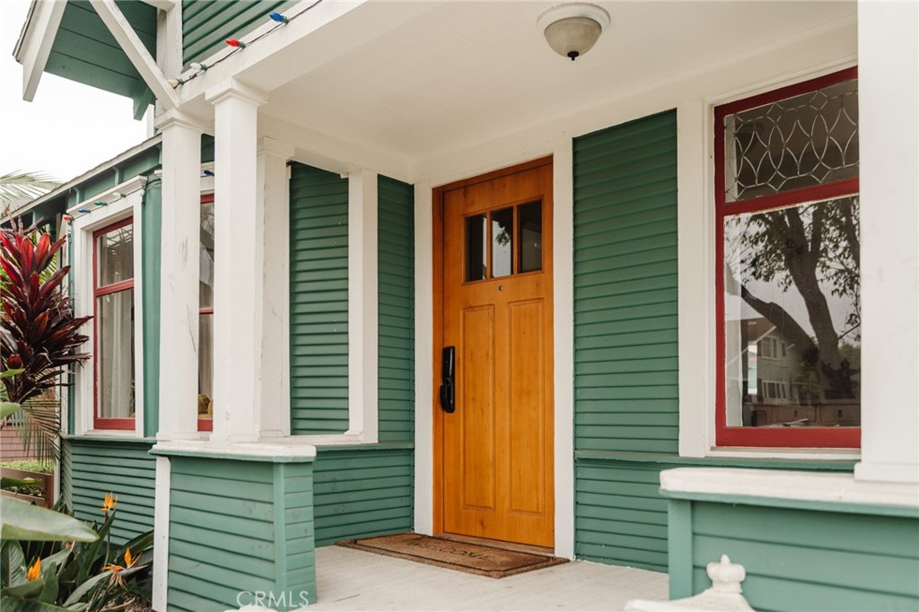 Covered front porch with green siding, white columns, an orange wood door, and decorative windows.