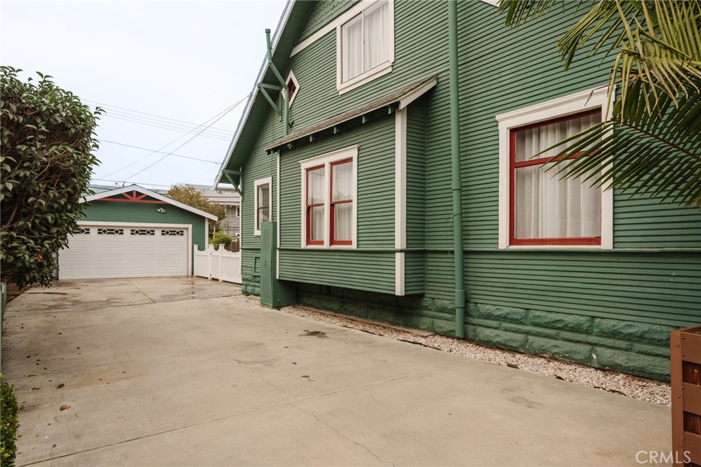 Green-sided house with red-trimmed windows beside a concrete driveway and detached garage.