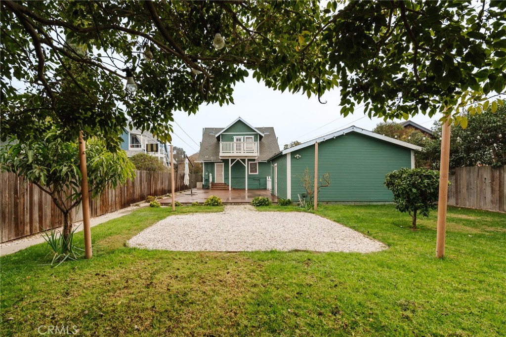 Rear view of a green house with a small deck, gravel patio, and fenced lawn.