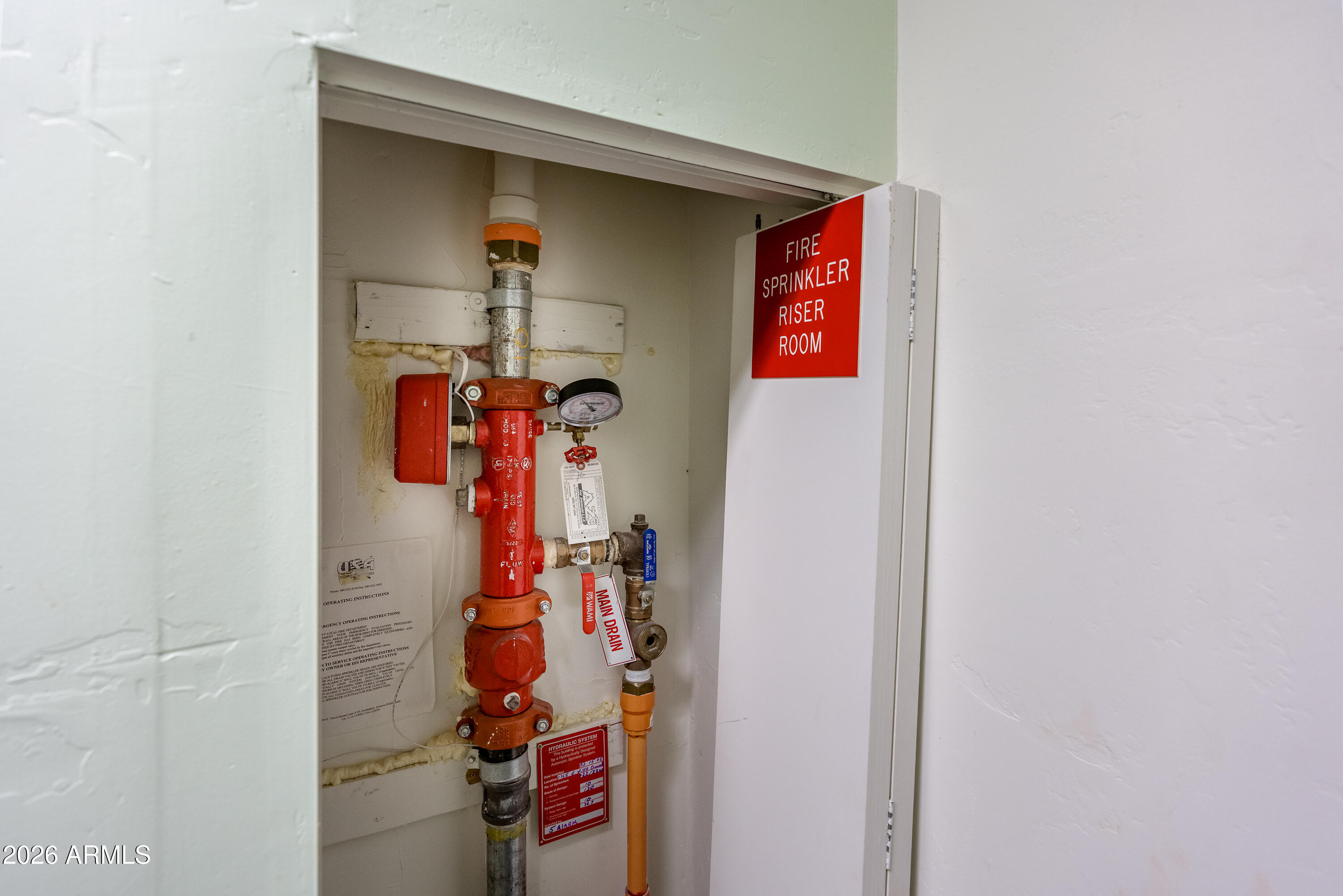 Fire sprinkler riser and main drain valves inside a labeled utility closet.