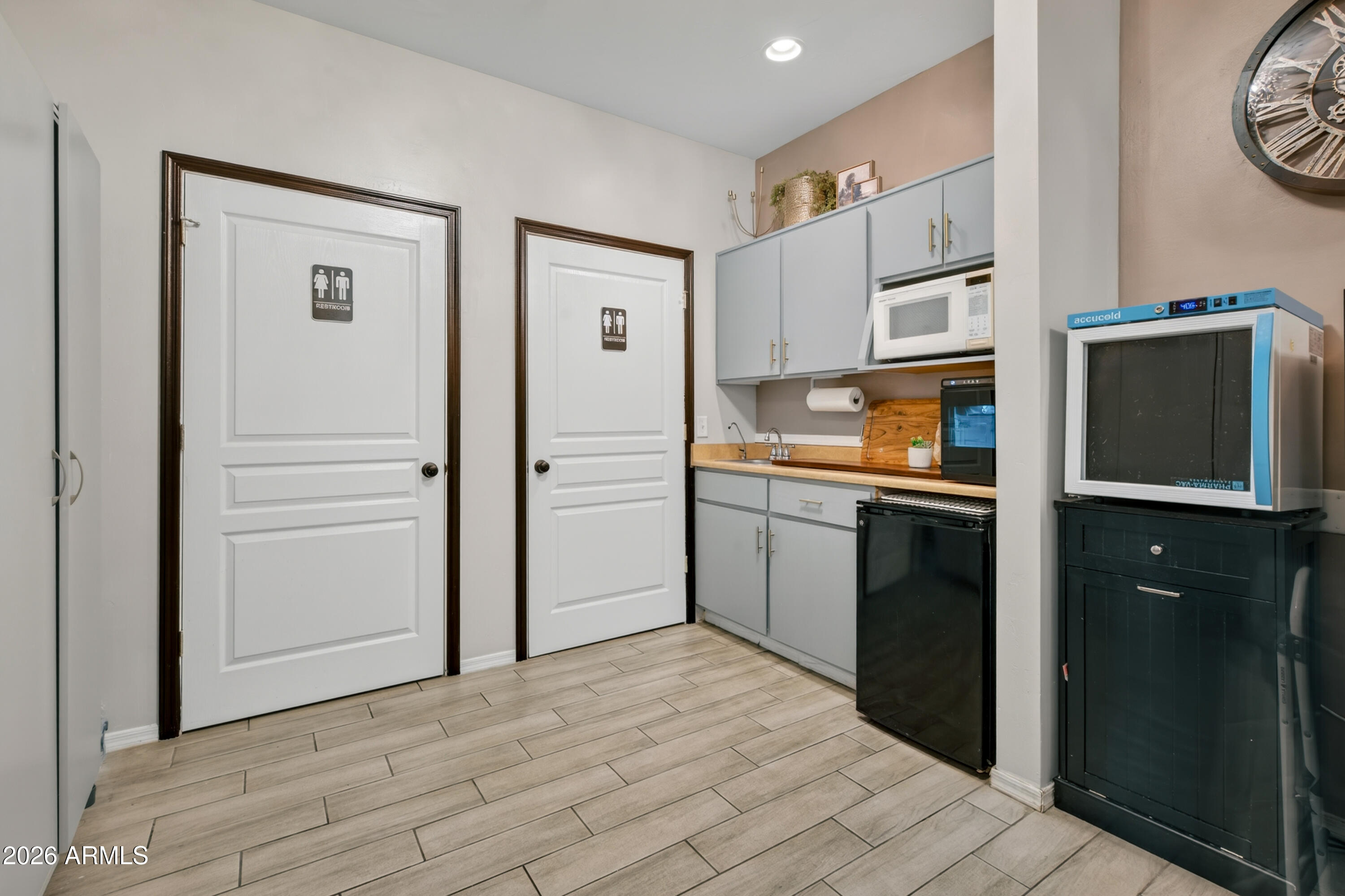 Kitchenette with gray cabinets, sink, microwave, black appliances, and two restroom doors.