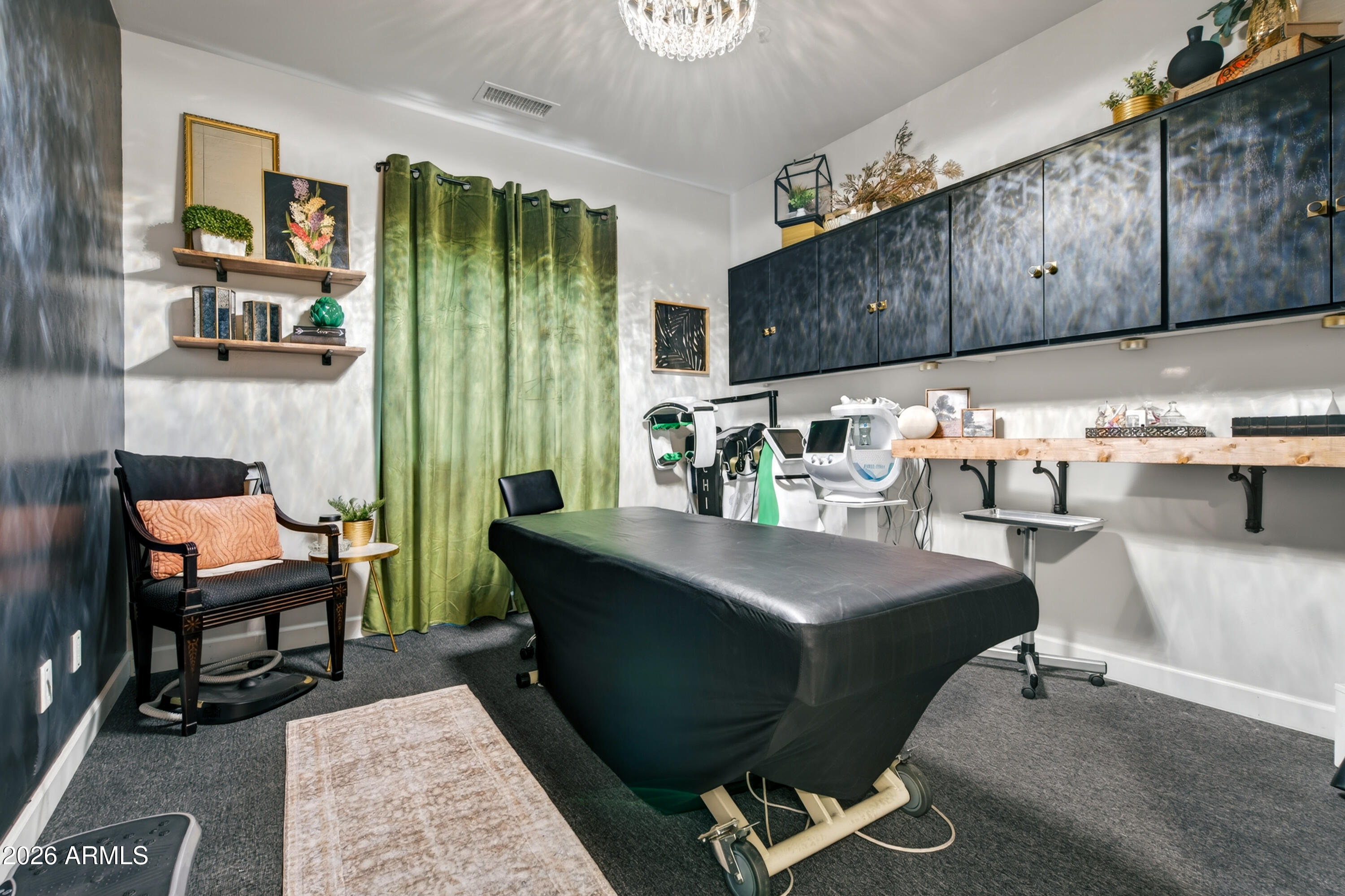 Treatment room with an adjustable black table, specialized equipment, dark cabinets, and green curtains.