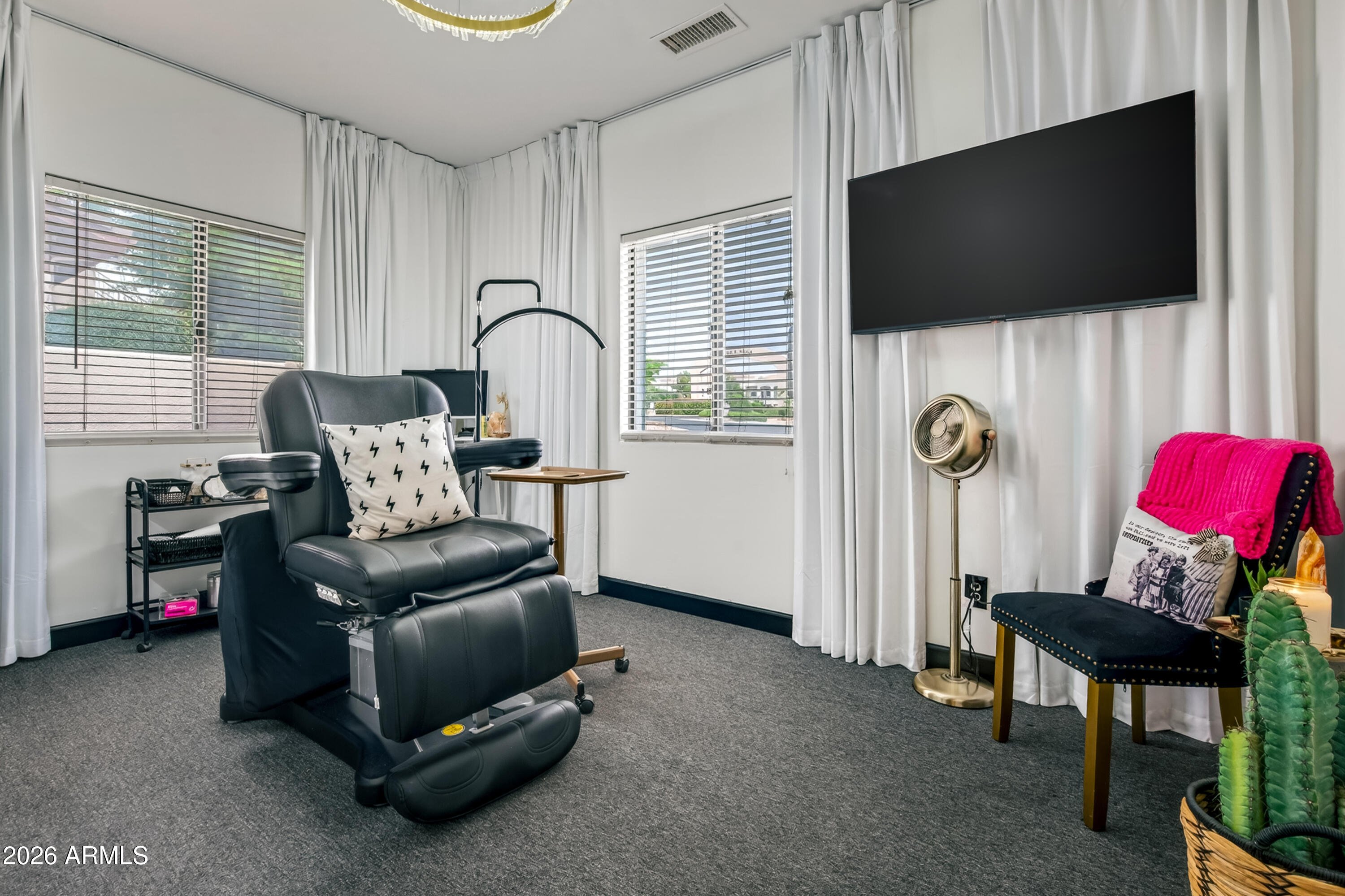 Furnished room with a black leather recliner, wall-mounted TV, and bright pink throw on an accent chair.