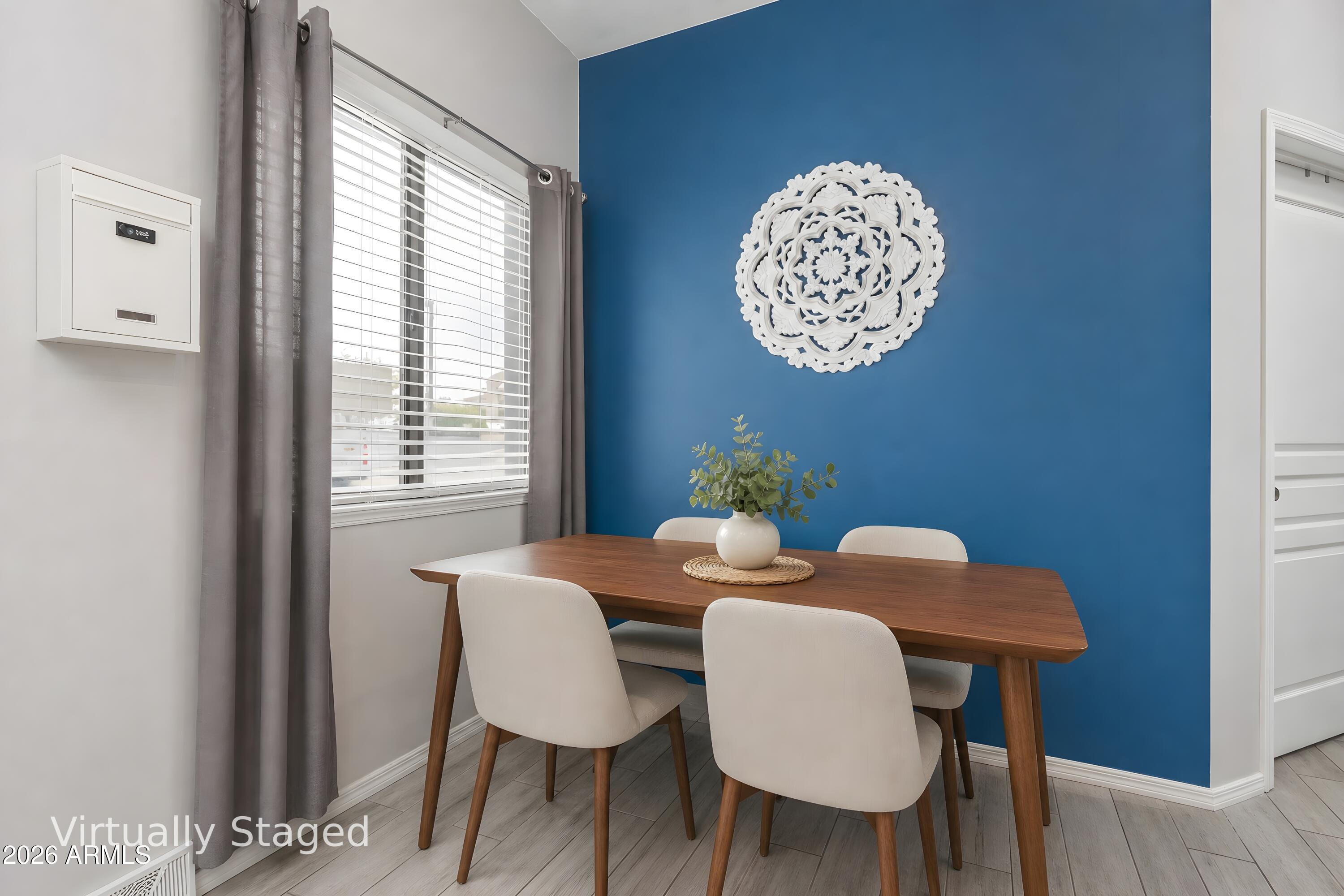 Dining area with a wood table, white chairs, and a blue accent wall, virtually staged.