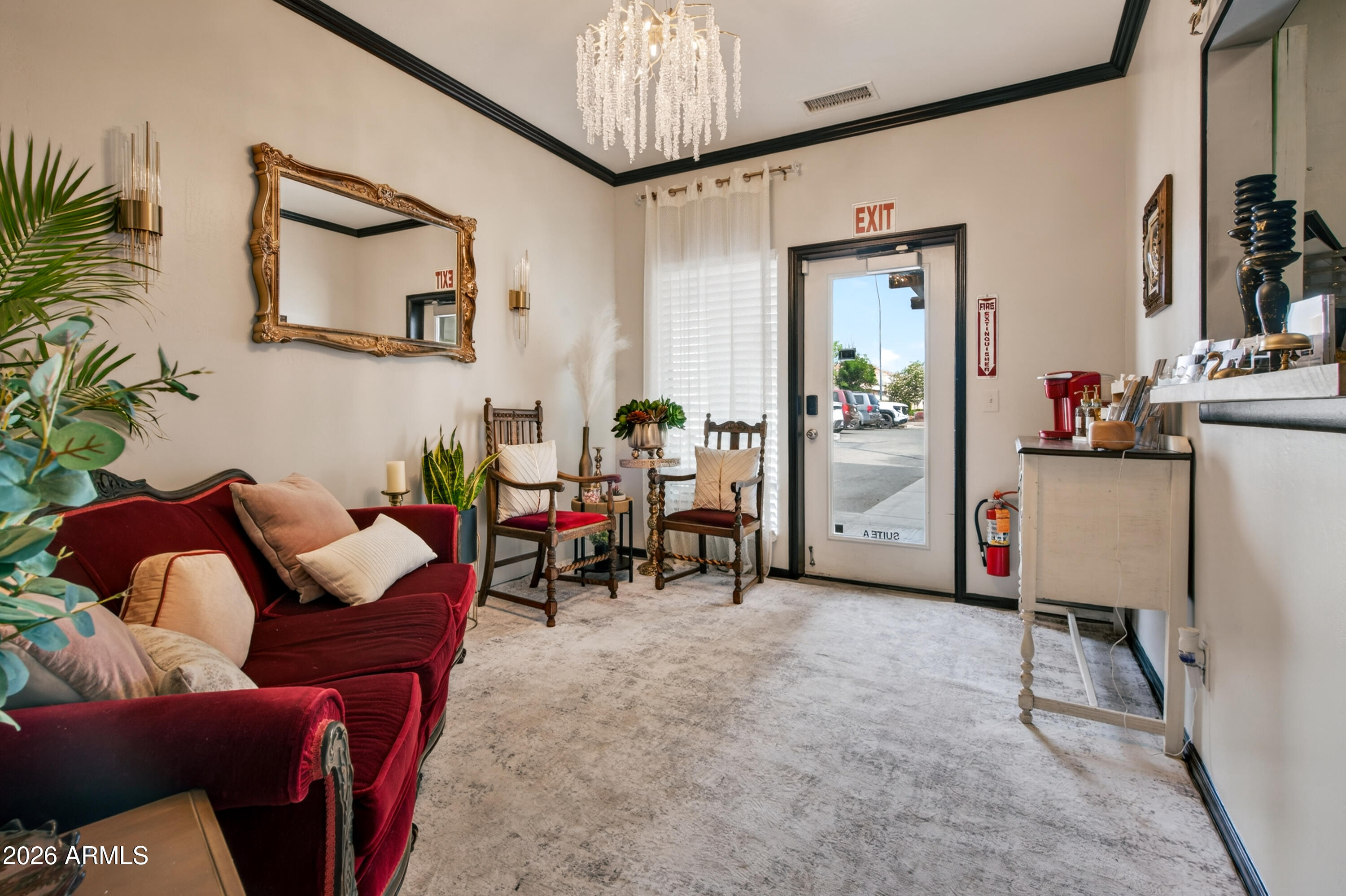 Furnished reception area with a burgundy sofa, ornate mirror, chandelier, and glass-front entry door.