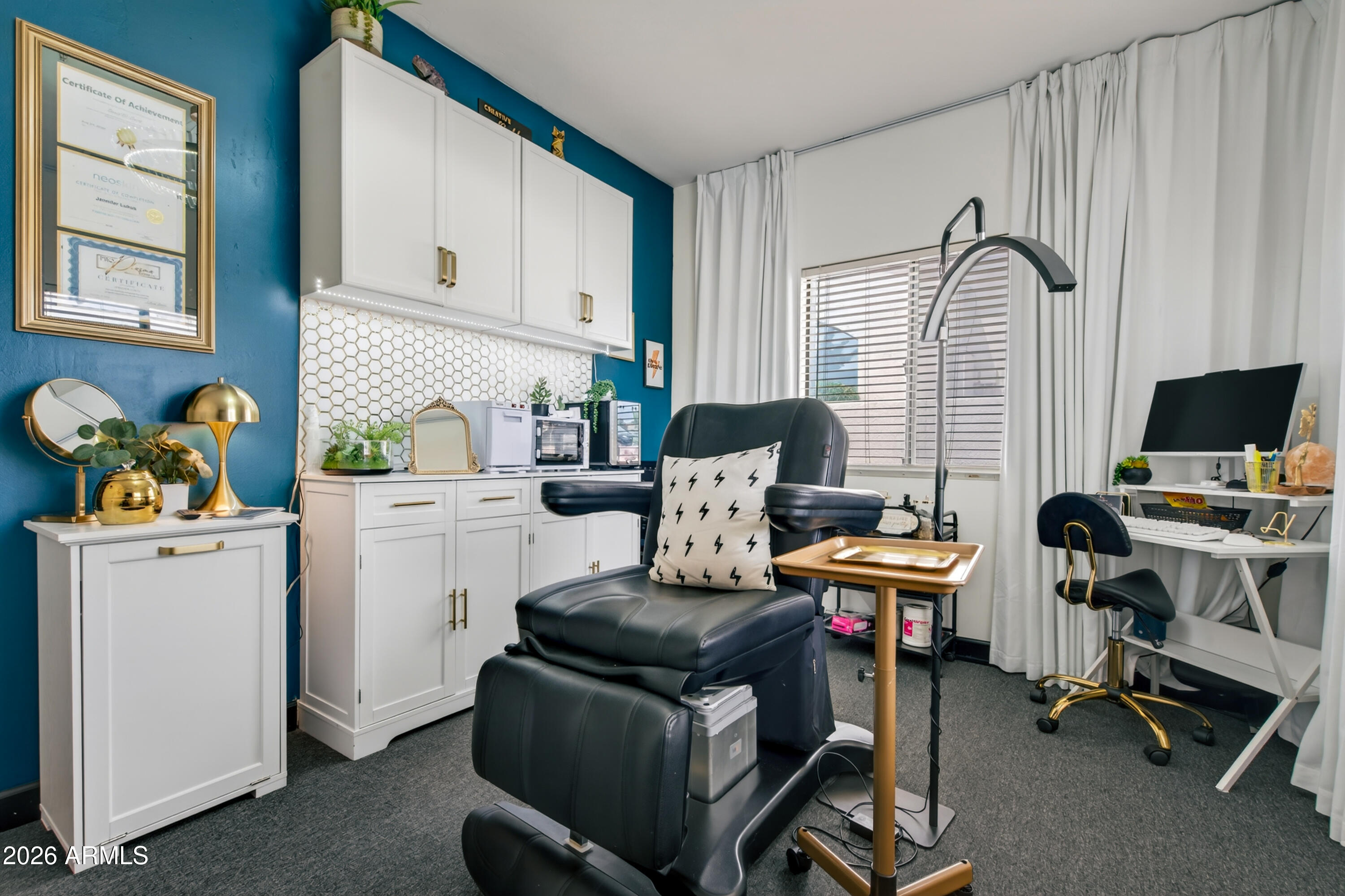 Furnished studio room with a black reclining chair, white cabinets, and a desk beside a window.