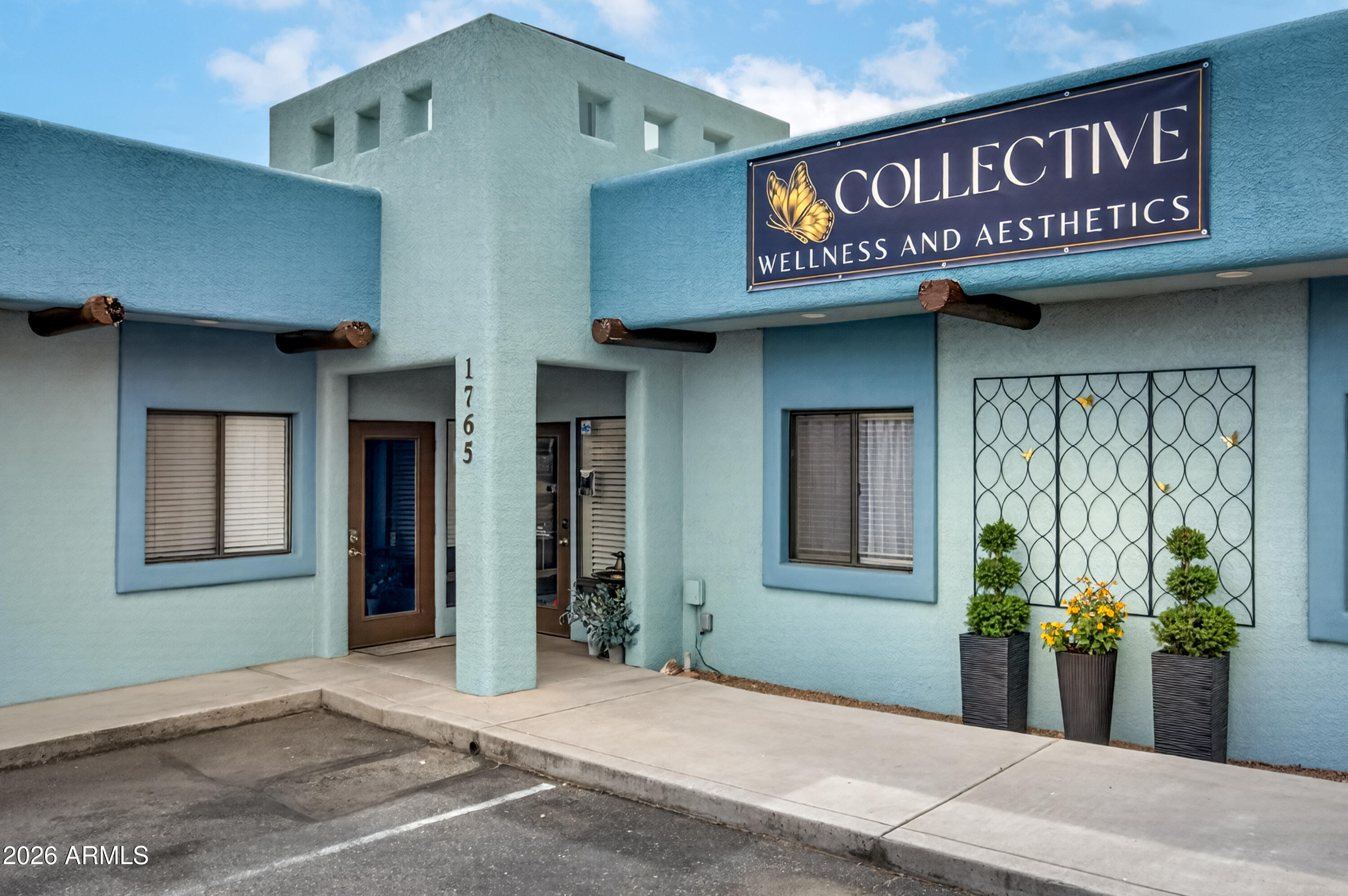 Light blue stucco storefront with a recessed entrance, potted plants, and a Collective Wellness and Aesthetics sign.