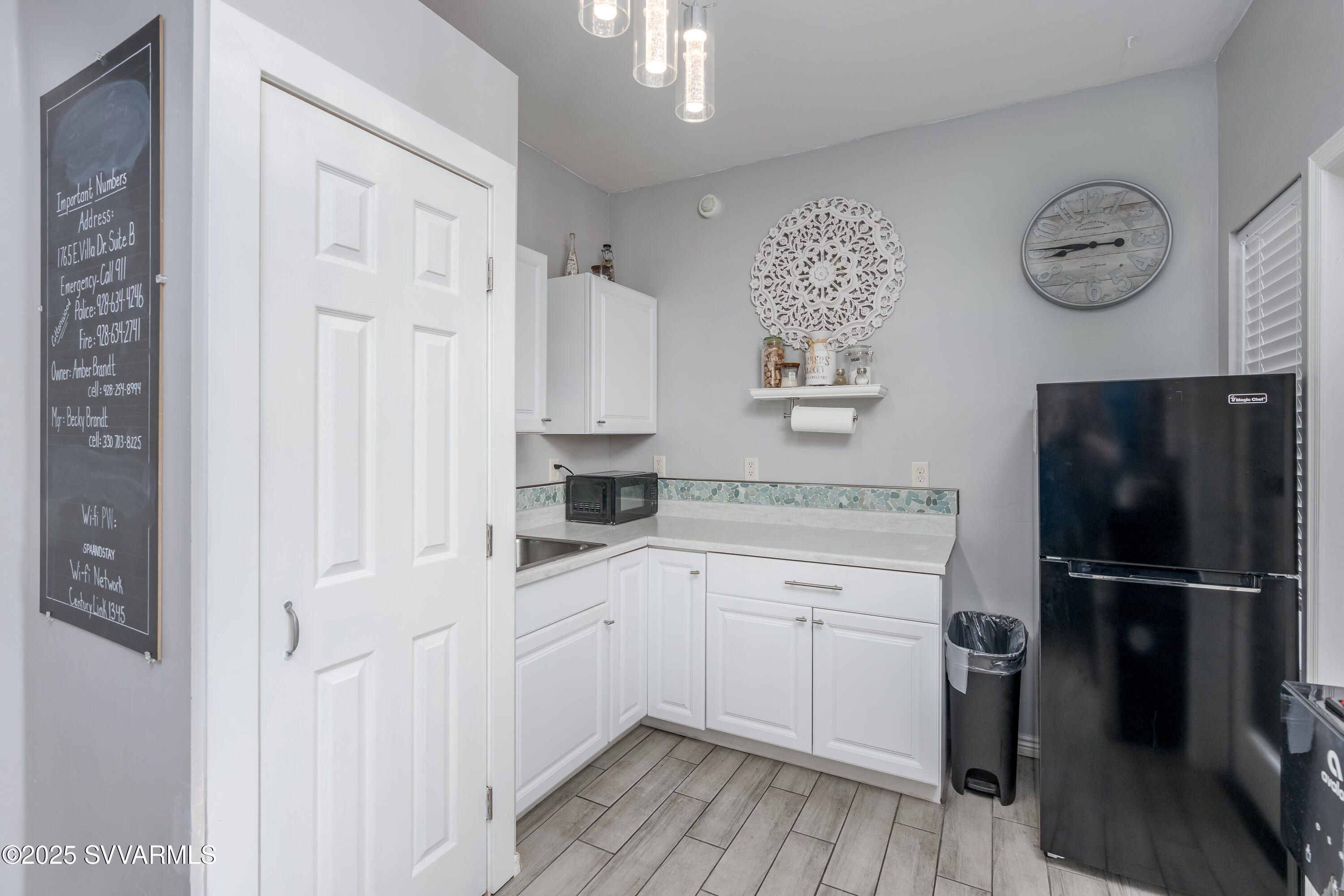 Compact kitchen with white cabinets, mosaic backsplash, black refrigerator, and gray tile flooring.