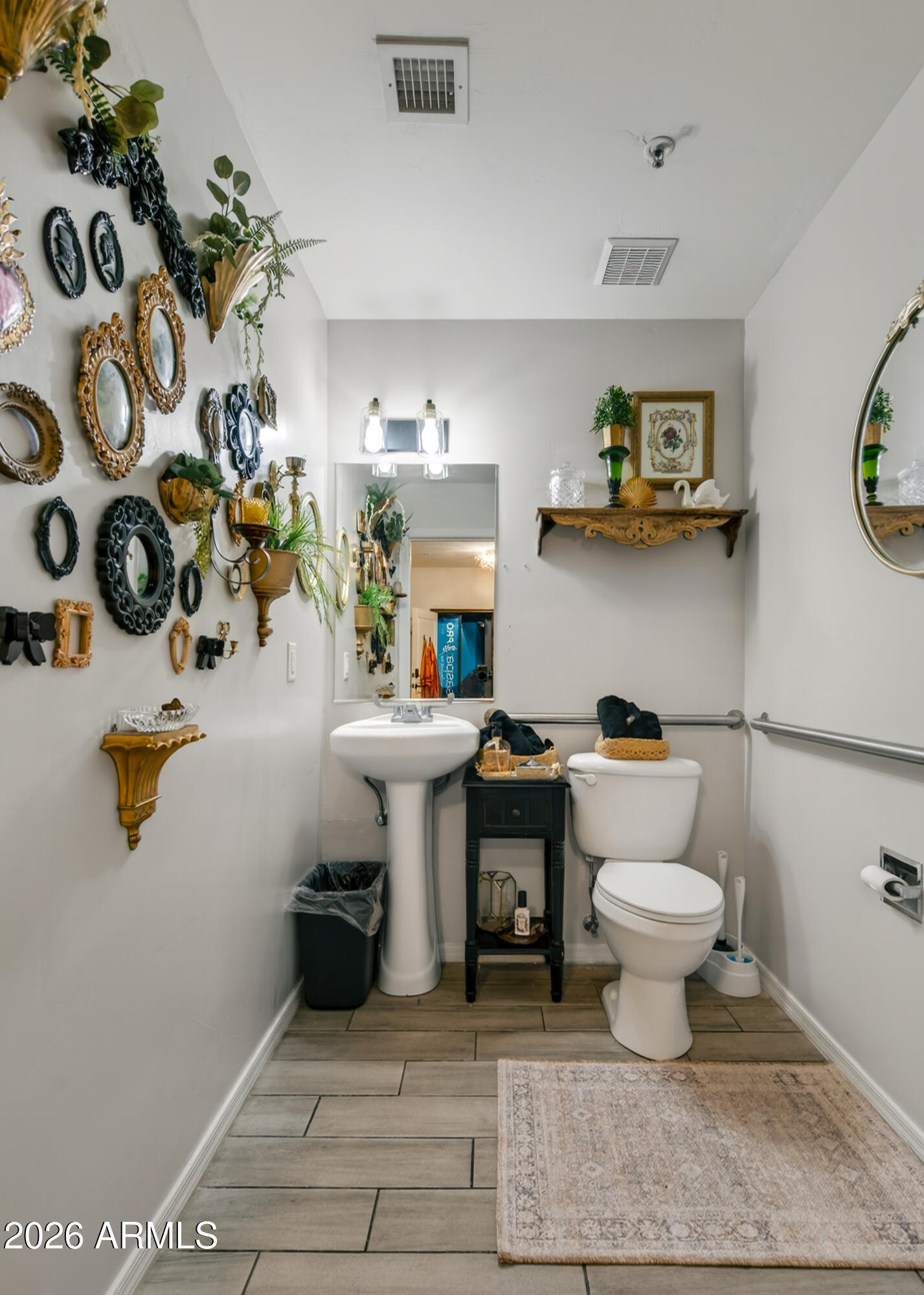 Bathroom with pedestal sink, toilet, grab bars, and an ornate collection of mirrors on the wall.