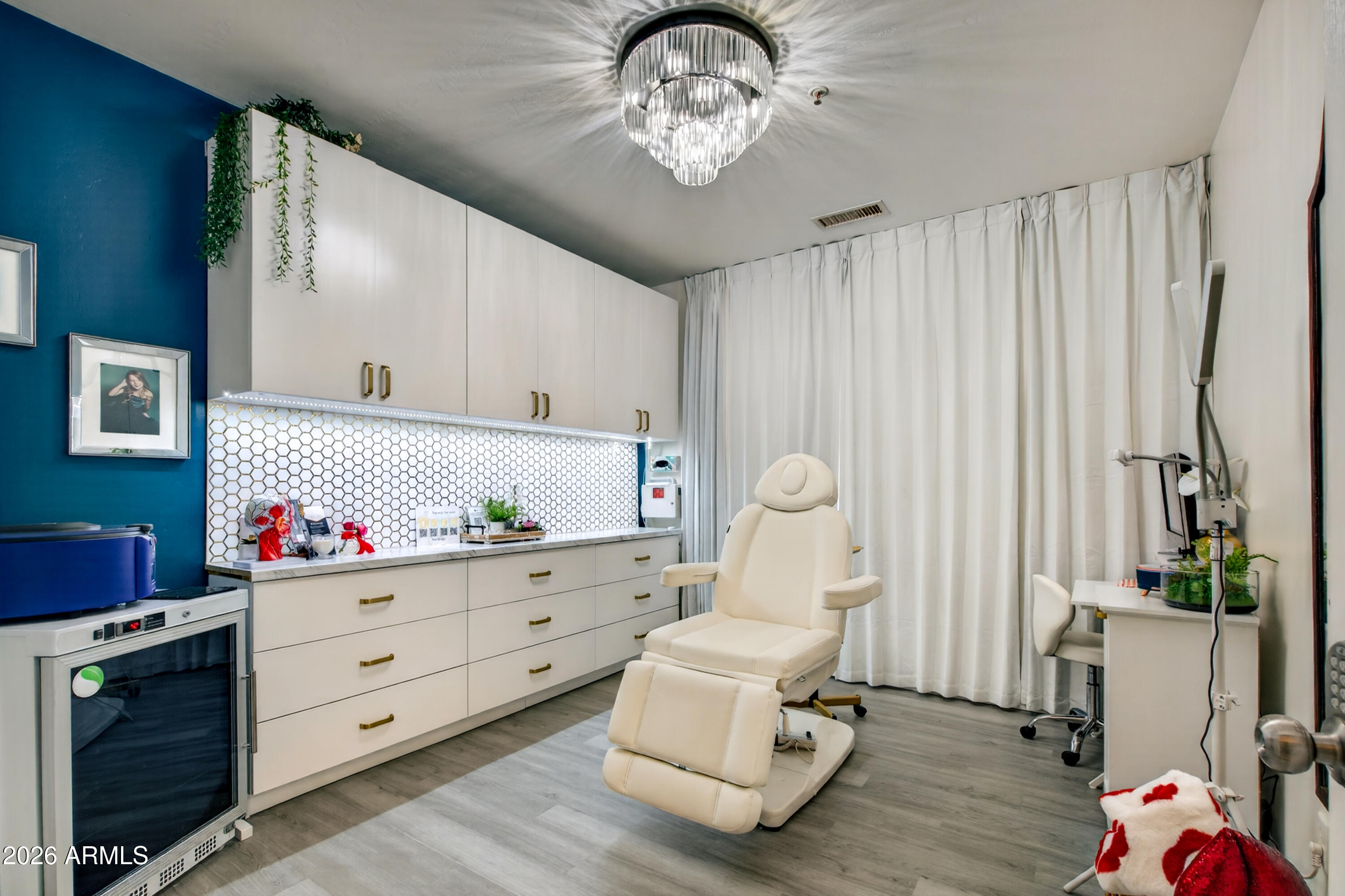 Treatment room with a cream reclining chair, white cabinetry, hexagonal tile backsplash, and blue accent wall.