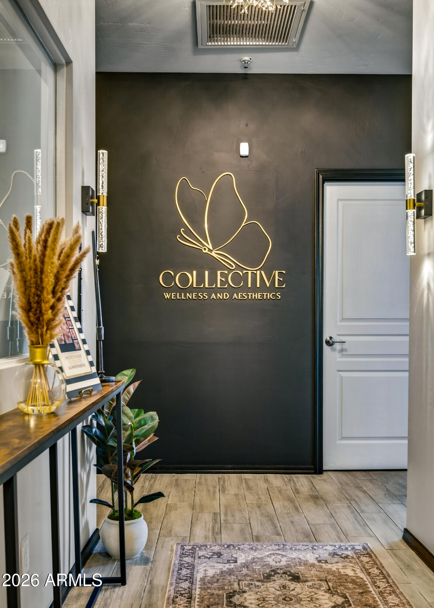 Wellness and aesthetics lobby with a gold wall logo, white door, and wood-look tile floor.