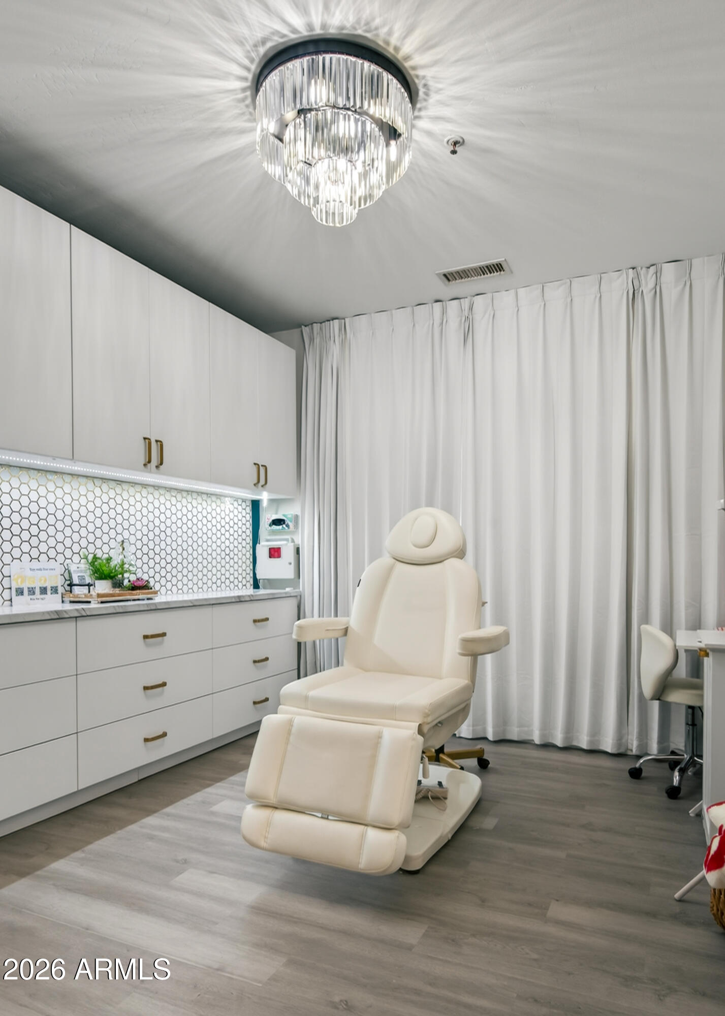 Treatment room with a cream reclining chair, white cabinetry, hexagonal tile backsplash, and full-length curtains.