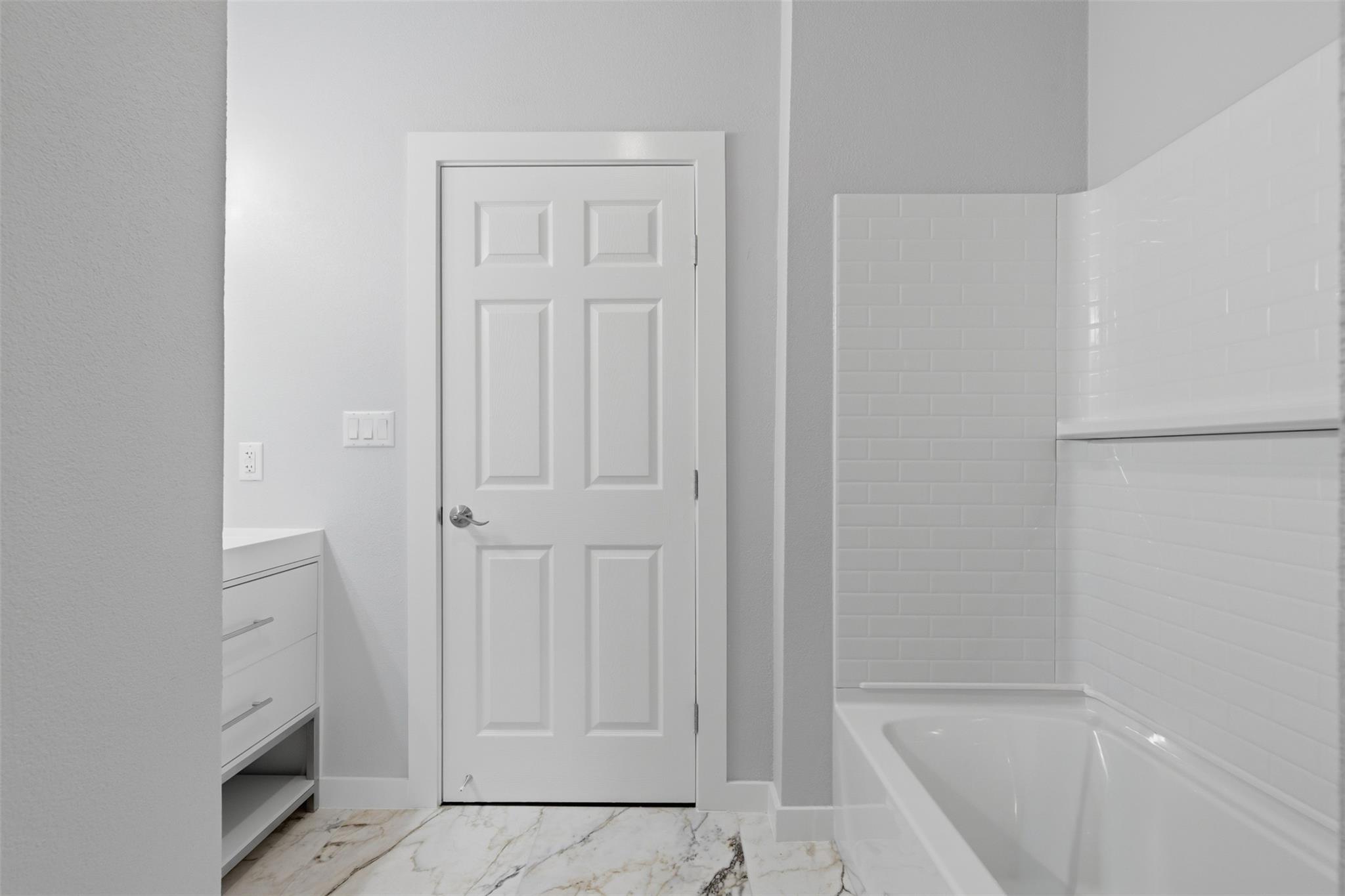 Bathroom with a white tiled bathtub and shower, marble-look floor, and paneled door.