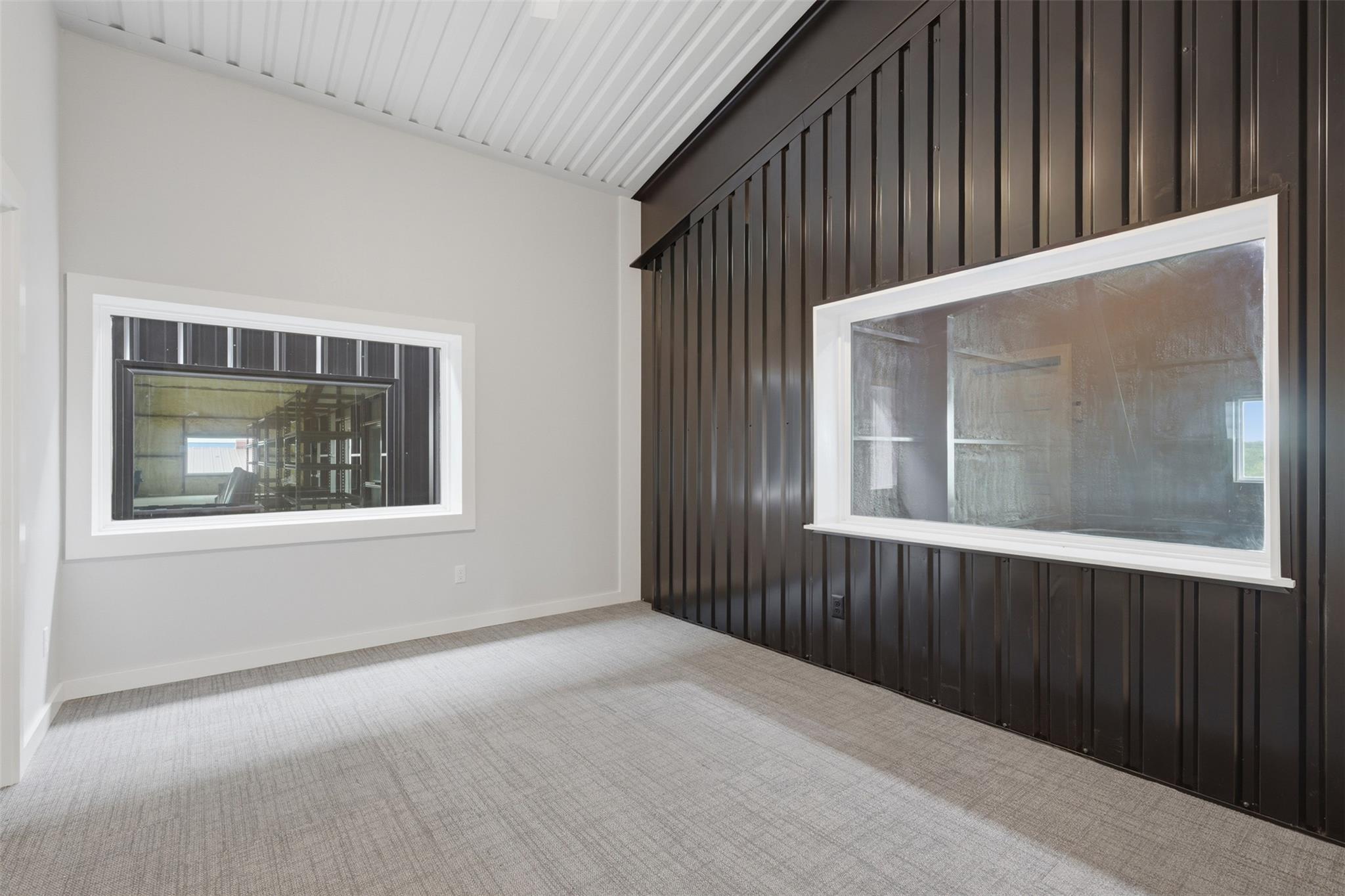Empty carpeted room with a vaulted ceiling, dark accent wall, and two interior windows.
