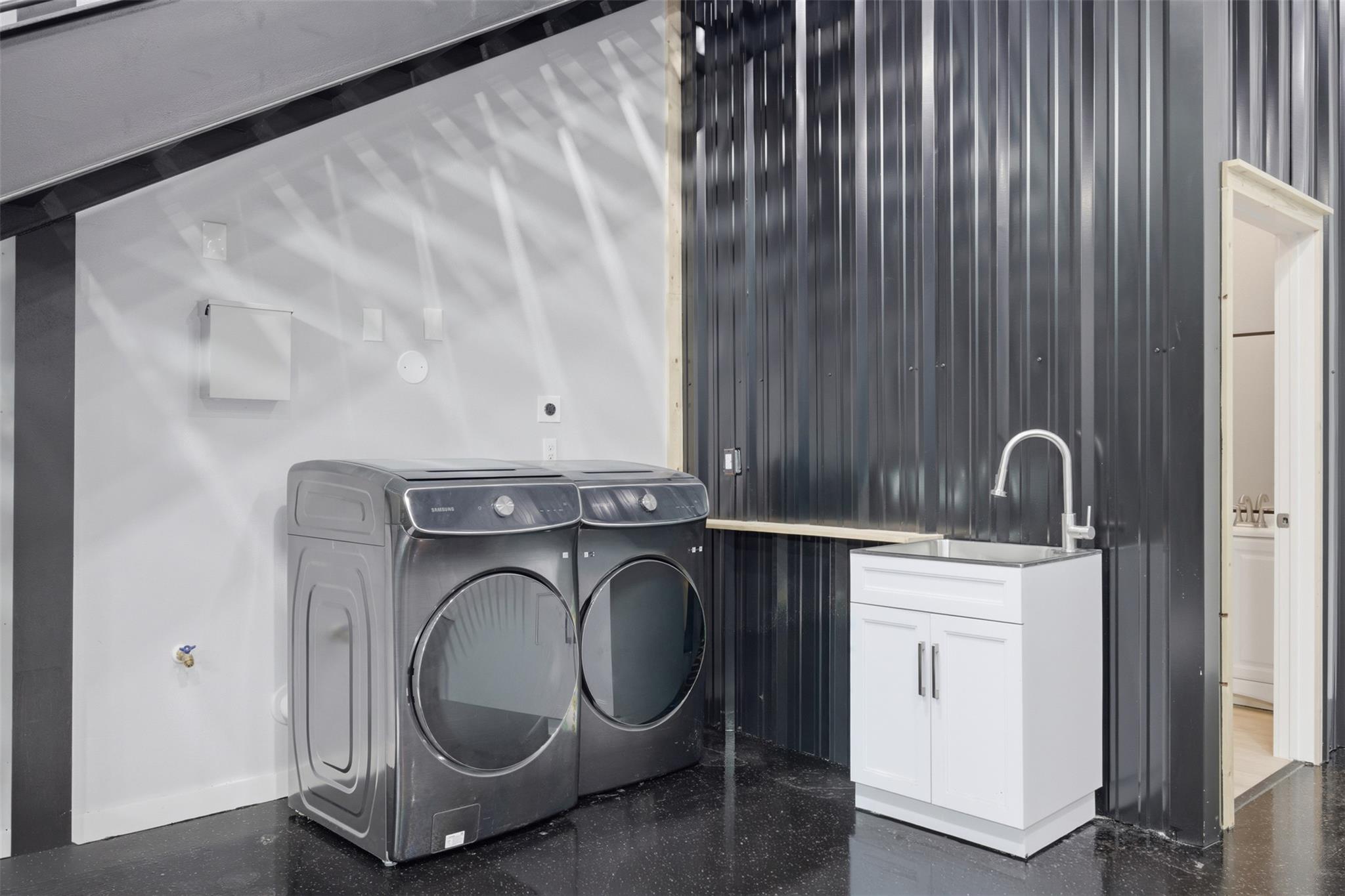 Laundry room with front-loading washer and dryer, utility sink, and black ribbed metal wall.