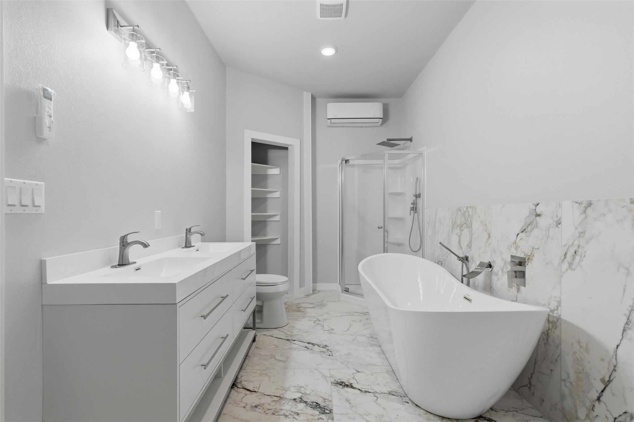 Modern bathroom with a double vanity, freestanding tub, marble-look tile, and glass-enclosed shower.